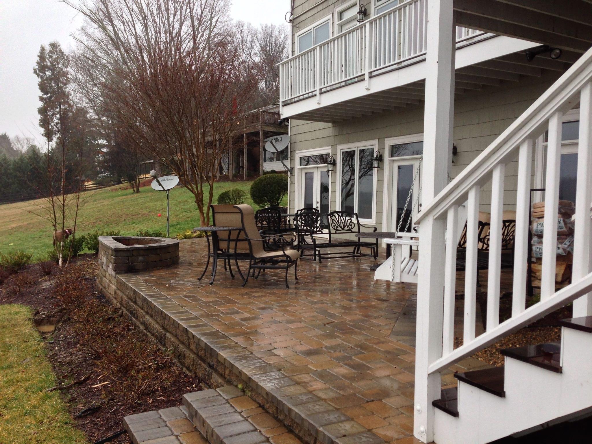 A residential patio with metal chairs, a swing, and a satellite dish. A grassy yard with trees and a distant structure.