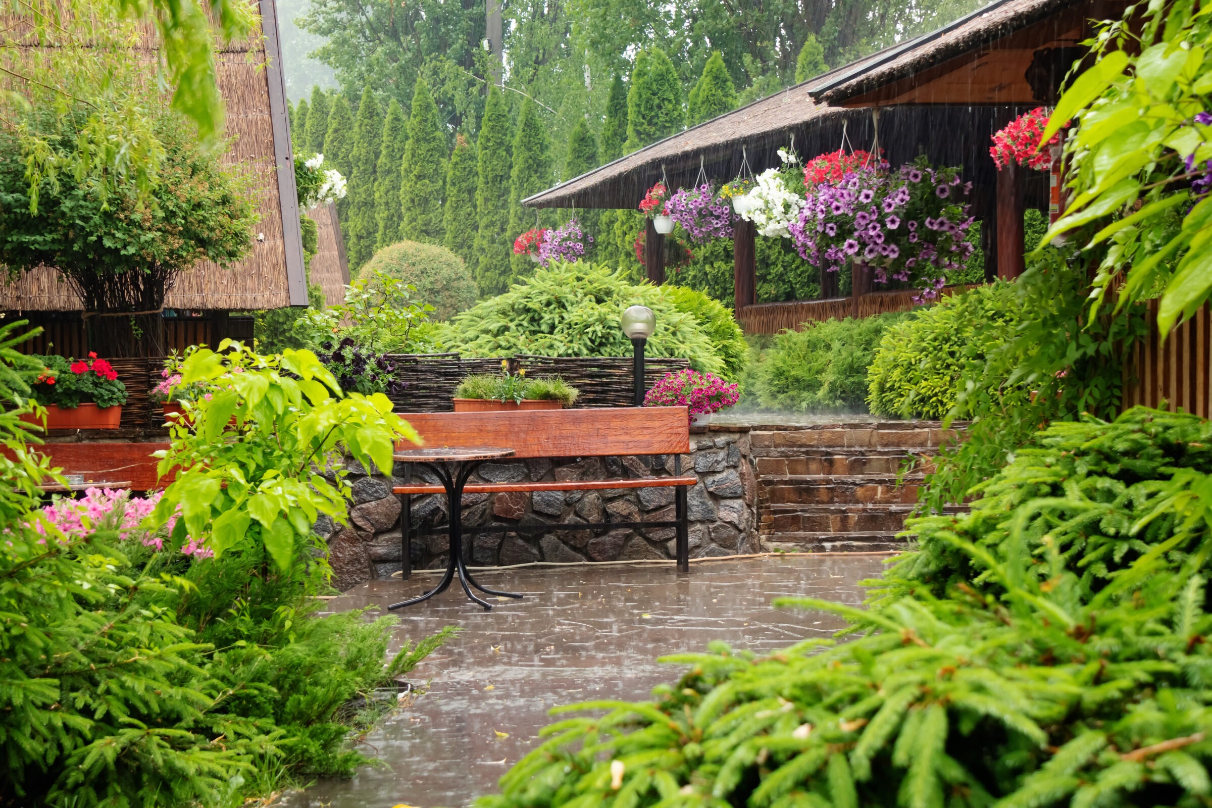 A serene garden scene in the rain, featuring lush greenery, a wooden bench, hanging flower baskets, and stone pathways creating a peaceful atmosphere.